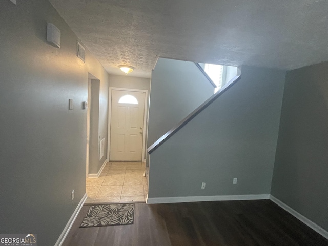 entrance foyer with light wood-style floors, visible vents, baseboards, and a textured ceiling