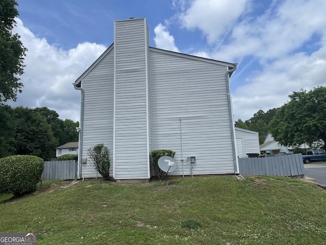 view of home's exterior with fence, a chimney, and a lawn
