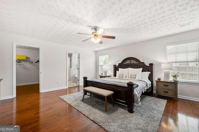 bedroom with a textured ceiling, baseboards, visible vents, wood finished floors, and a spacious closet