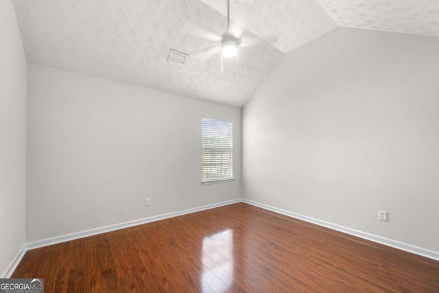 empty room with a textured ceiling, visible vents, ceiling fan, vaulted ceiling, and wood finished floors