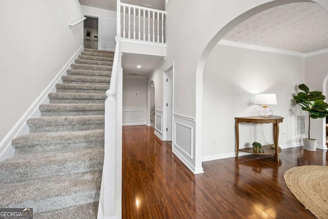foyer entrance with ornamental molding, visible vents, wood finished floors, arched walkways, and stairway