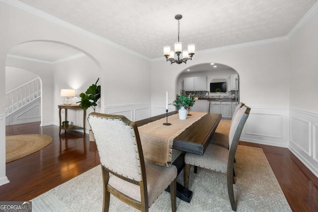 dining area featuring a notable chandelier, a decorative wall, wood finished floors, arched walkways, and stairway