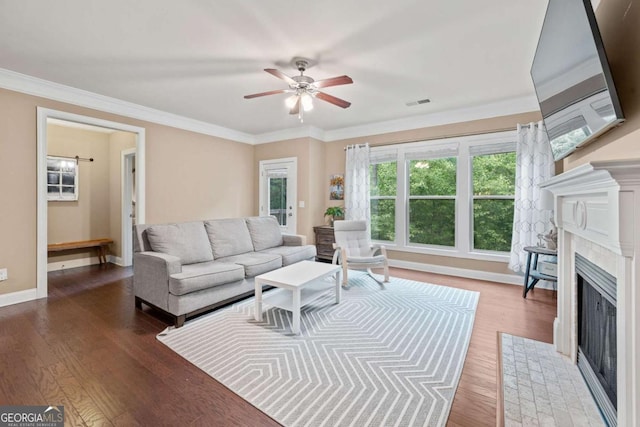 living room with wood finished floors, ornamental molding, a ceiling fan, baseboards, and a fireplace with flush hearth