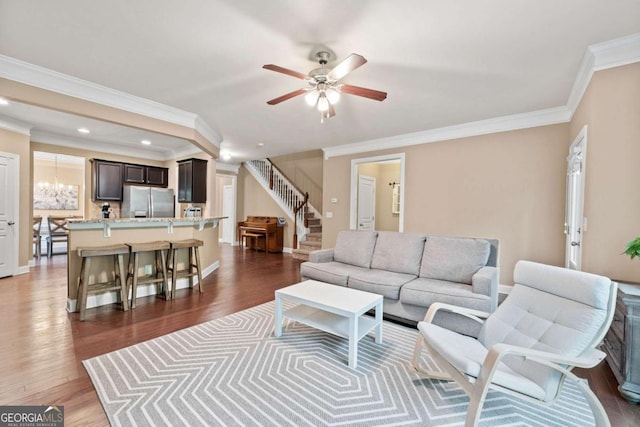 living room with stairs, ornamental molding, wood finished floors, and ceiling fan with notable chandelier