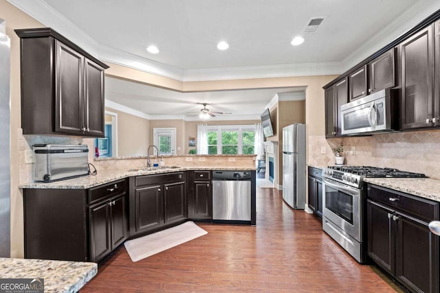 kitchen with a peninsula, wood finished floors, a sink, appliances with stainless steel finishes, and ornamental molding