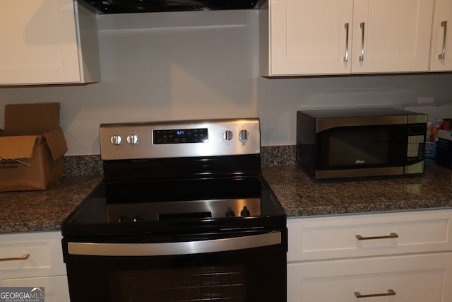 kitchen with black electric range oven, stainless steel microwave, white cabinetry, and dark stone counters