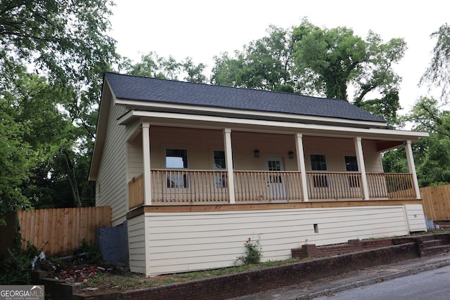 view of front of house featuring covered porch, a shingled roof, and fence