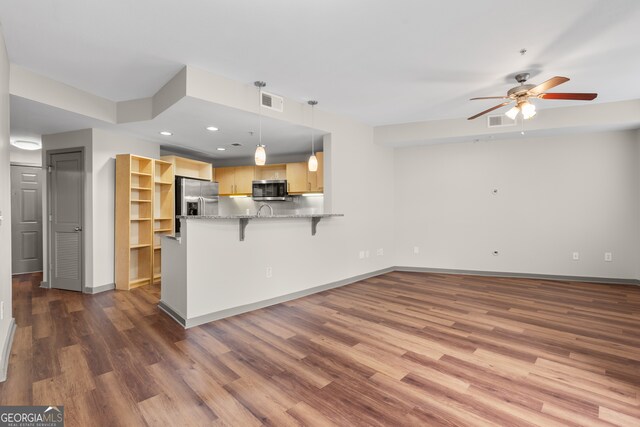 kitchen with a ceiling fan, light brown cabinets, a peninsula, wood finished floors, and appliances with stainless steel finishes