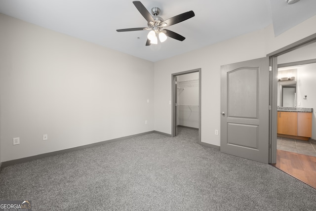 unfurnished bedroom with a closet, light carpet, baseboards, and a spacious closet