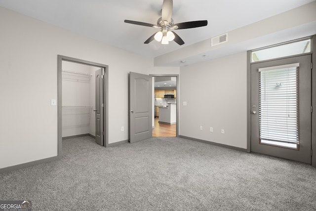 unfurnished bedroom with a walk in closet, visible vents, baseboards, ceiling fan, and light carpet