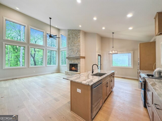 kitchen featuring light stone countertops, a sink, a kitchen island with sink, stainless steel appliances, and a fireplace