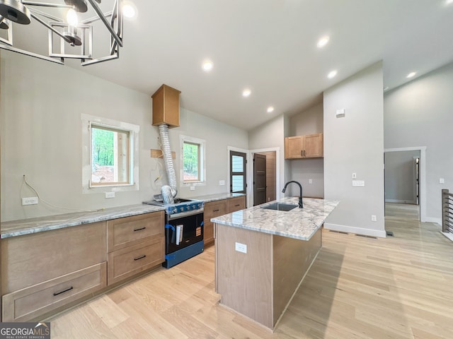 kitchen with light wood finished floors, a sink, a kitchen island with sink, light stone countertops, and range with gas stovetop