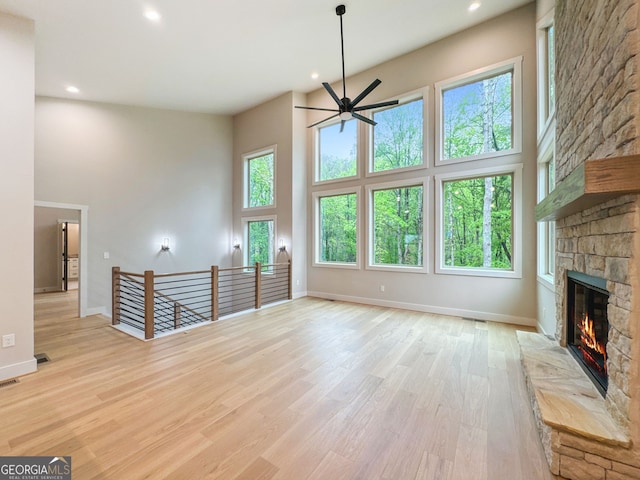 unfurnished living room with a ceiling fan, a high ceiling, a fireplace, baseboards, and recessed lighting