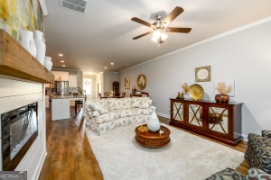 living area featuring a ceiling fan, a fireplace, dark wood finished floors, visible vents, and ornamental molding