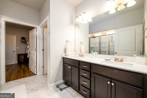 bathroom featuring a sink, marble finish floor, a stall shower, double vanity, and baseboards