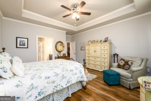 bedroom featuring a ceiling fan, a raised ceiling, crown molding, and wood finished floors