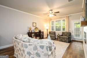 living area featuring baseboards, dark wood-style flooring, ceiling fan, and crown molding