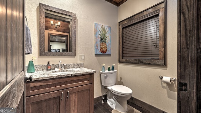 half bath with toilet, wood finished floors, baseboards, a textured wall, and vanity
