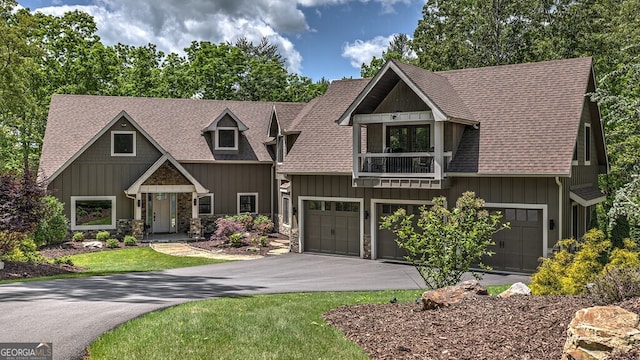 craftsman inspired home with stone siding, an attached garage, aphalt driveway, a balcony, and roof with shingles