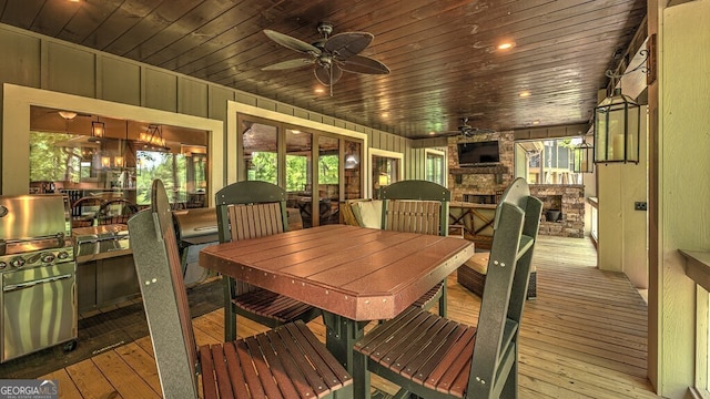 dining area featuring wood walls, hardwood / wood-style floors, wooden ceiling, a ceiling fan, and a stone fireplace