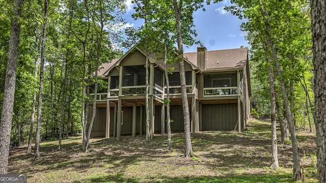 rear view of property with a chimney, a sunroom, and a shingled roof