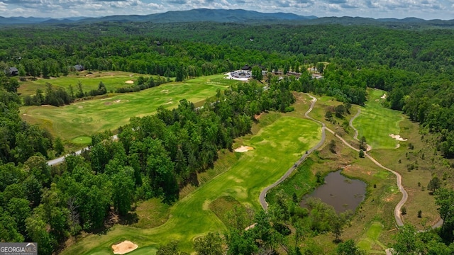 drone / aerial view with a water and mountain view, a wooded view, and golf course view