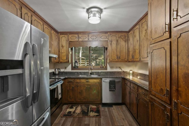kitchen with a sink, stainless steel appliances, brown cabinets, under cabinet range hood, and dark wood-style floors