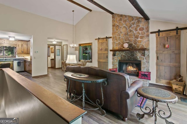 living area with a barn door, a fireplace, light wood-style flooring, beamed ceiling, and baseboards