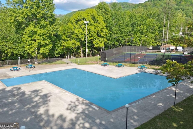 view of swimming pool with a view of trees and fence