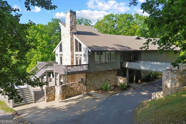 view of front of home featuring stone siding, roof with shingles, a chimney, and stairs