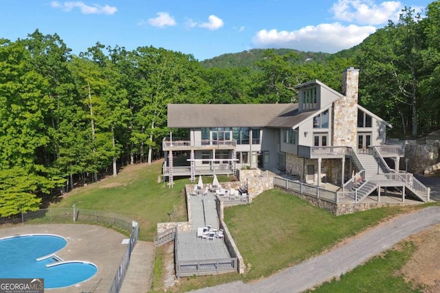rear view of house with a chimney, a lawn, a deck, a forest view, and stairs