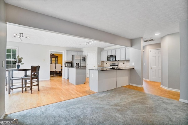 1314 Durham Ter, Mcdonough, GA 30252 - kitchen with stainless steel appliances, light carpet, a peninsula, dark countertops, and light wood-style floors
