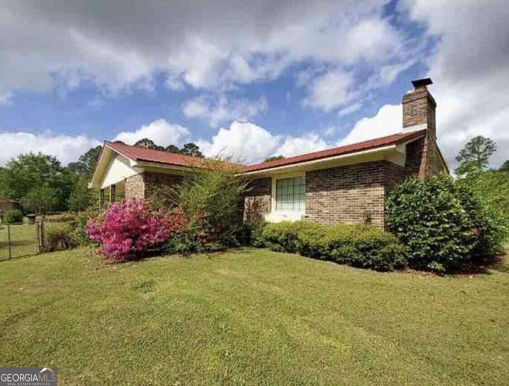 view of side of home featuring brick siding, a chimney, a lawn, and fence