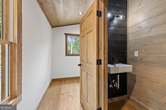 corridor featuring light wood-style flooring, baseboards, a sink, wooden walls, and crown molding