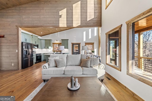 living area featuring light wood finished floors, wood walls, visible vents, and high vaulted ceiling