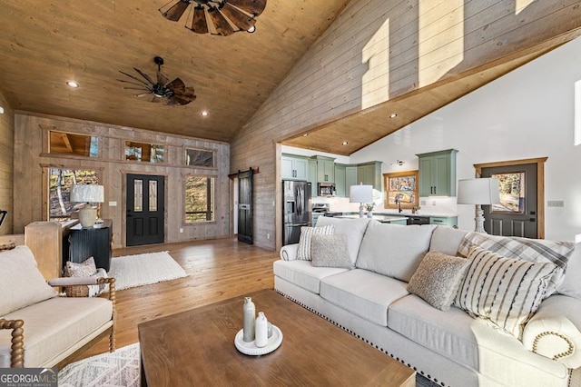 living area with wood ceiling, light wood-style flooring, high vaulted ceiling, wood walls, and ceiling fan