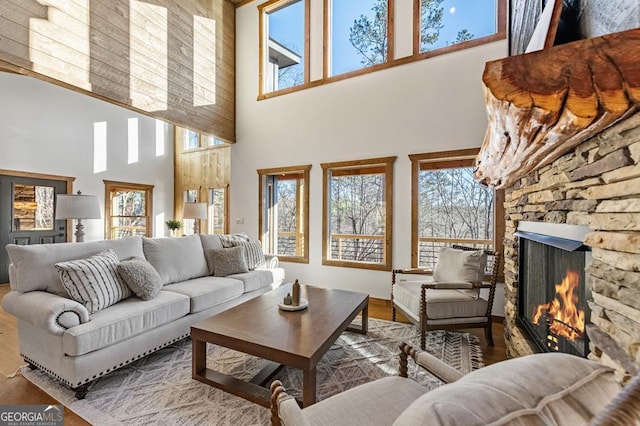 living area featuring wood finished floors, a towering ceiling, and a stone fireplace