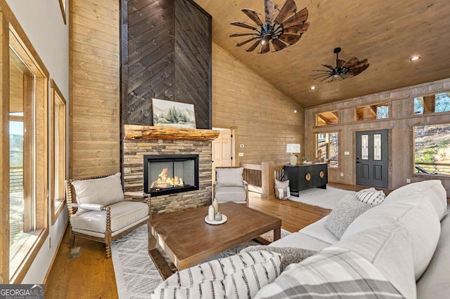 living room featuring a stone fireplace, wood walls, high vaulted ceiling, and wood finished floors