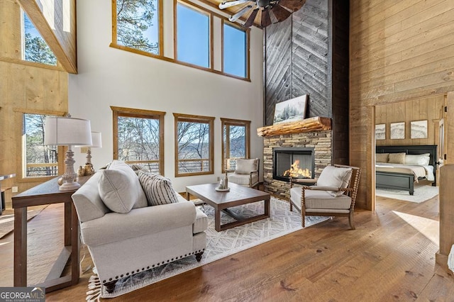 living area with a high ceiling, hardwood / wood-style floors, a stone fireplace, and a ceiling fan
