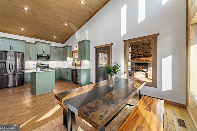 kitchen with green cabinetry, high vaulted ceiling, light wood finished floors, light countertops, and appliances with stainless steel finishes