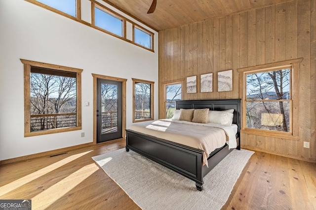 bedroom with multiple windows, a towering ceiling, wood-type flooring, wood ceiling, and access to exterior