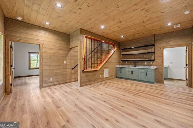 unfurnished living room featuring a sink, light wood-type flooring, wooden ceiling, stairway, and wooden walls