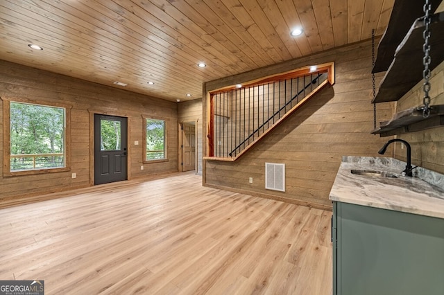 unfurnished living room featuring a sink, stairs, visible vents, wooden ceiling, and wooden walls