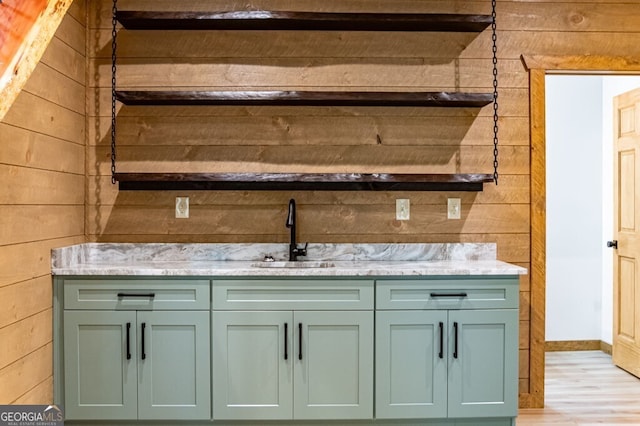bar with a sink, wooden walls, baseboards, and light wood-style flooring