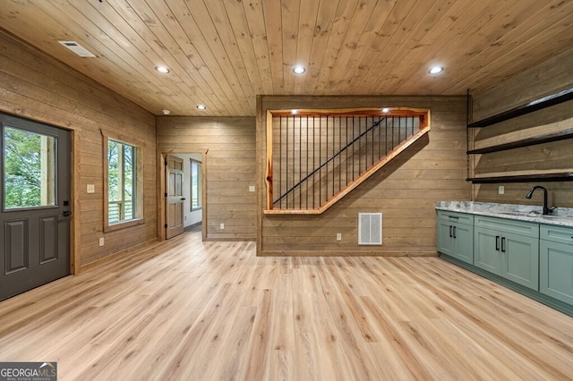 unfurnished living room with light wood-style flooring, a sink, visible vents, wood walls, and wooden ceiling