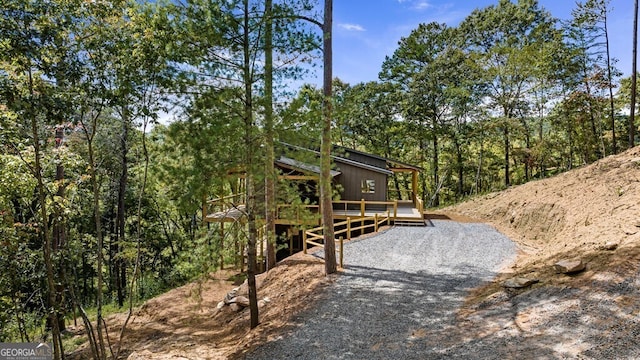 exterior space featuring a deck, gravel driveway, and a view of trees