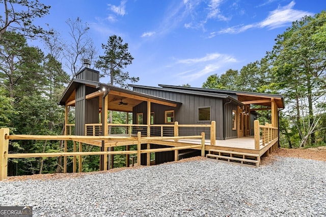 back of property with a deck, a ceiling fan, a chimney, and board and batten siding