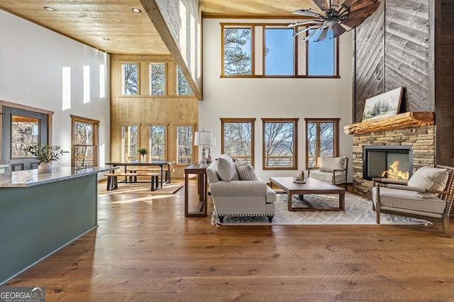 living area featuring a stone fireplace, plenty of natural light, hardwood / wood-style floors, and a high ceiling