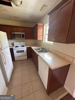 kitchen featuring a sink, white appliances, light countertops, and light tile patterned floors