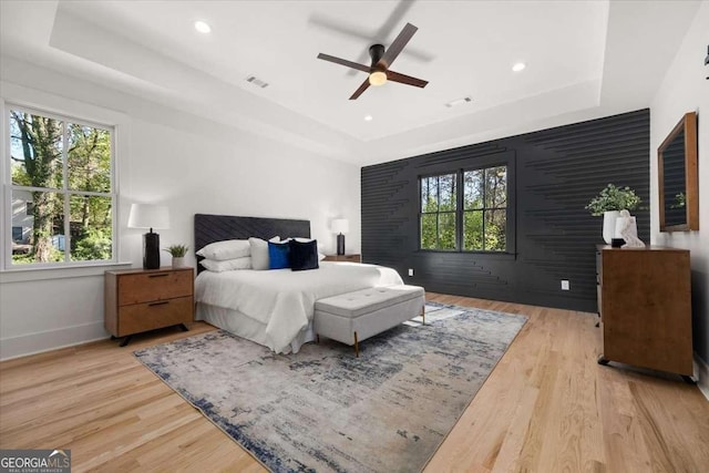 bedroom with baseboards, a raised ceiling, light wood-style flooring, and visible vents